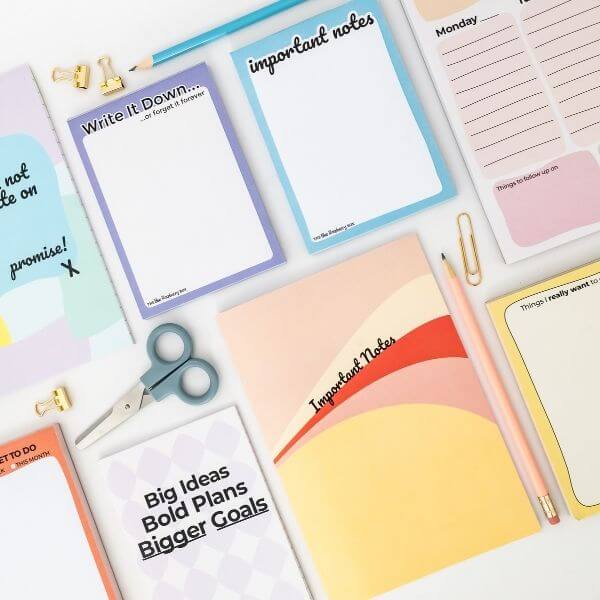 Collection of colorful notepads with various messages and a pair of scissors on a white background.