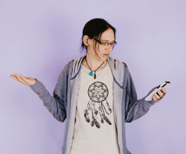Jeni wearing a t-shirt with a dreamcatcher design and purple hoodie, holding a phone, on a light purple background